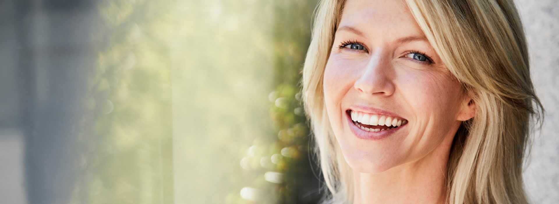A woman is smiling after dental crowns & bridges treatment.